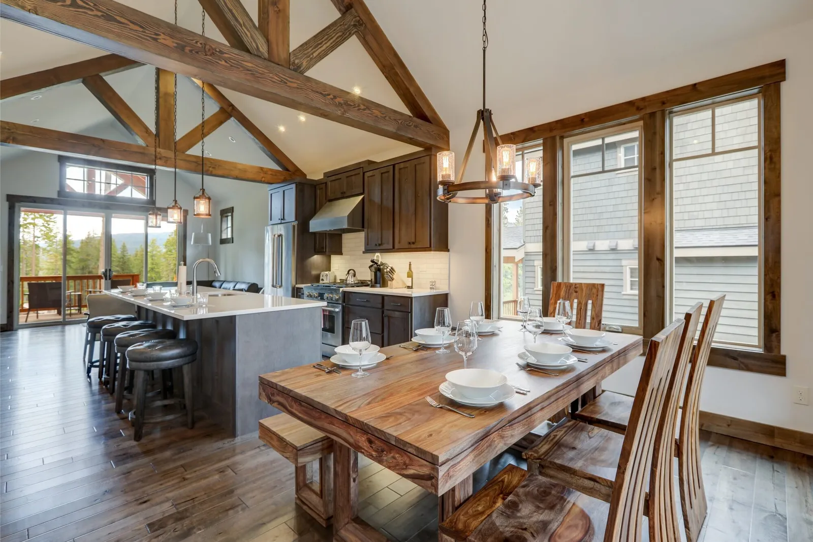 Box beam trusses over an open kitchen and dining room with a stone fireplace and a plank table