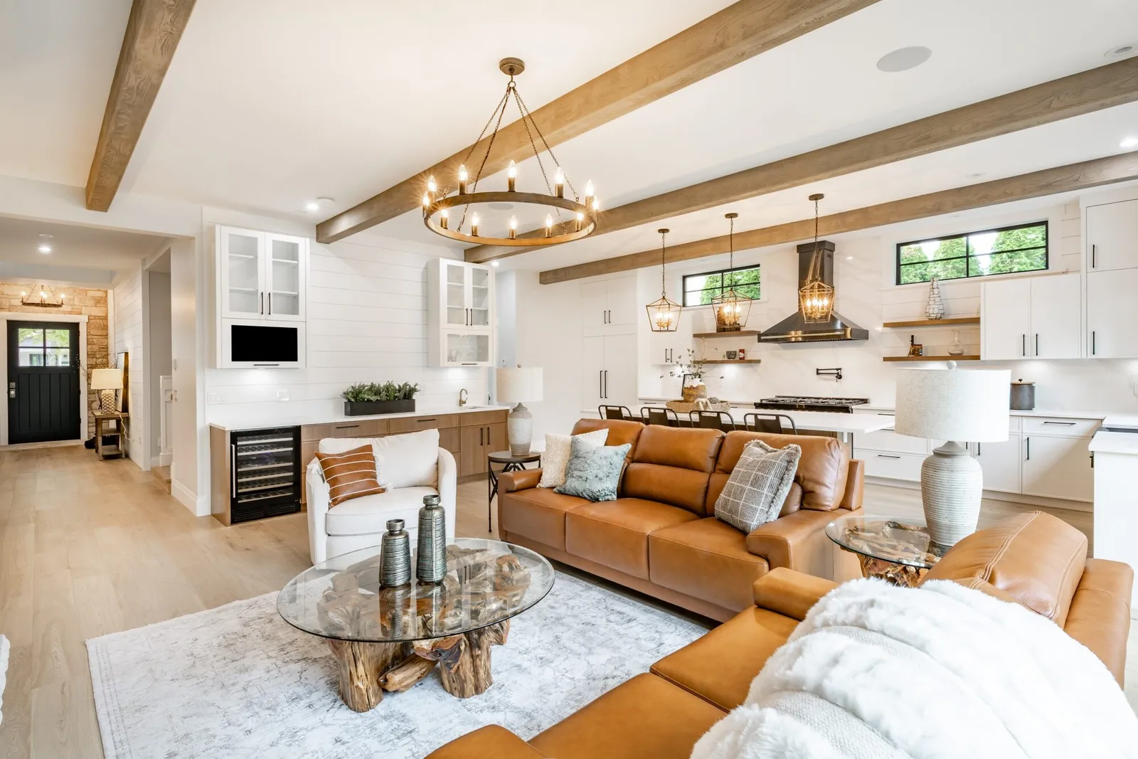 Wood box beams running across a white ceiling in an open living room, with the kitchen beyond
