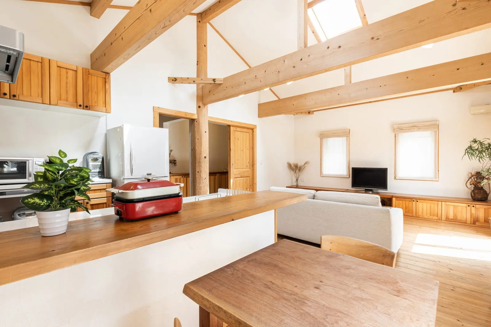 White pine beams and an exposed truss above a kitchen bar opening onto a living room