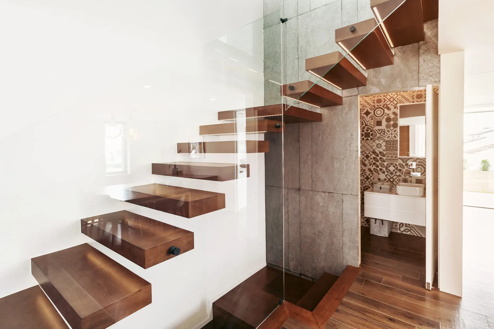 Floating walnut stair treads with a glass balustrade in a modern concrete entryway