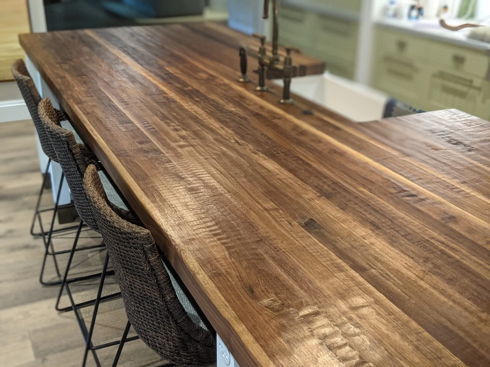 Character-grade walnut plank countertop along an island with a farmhouse sink and woven counter stools