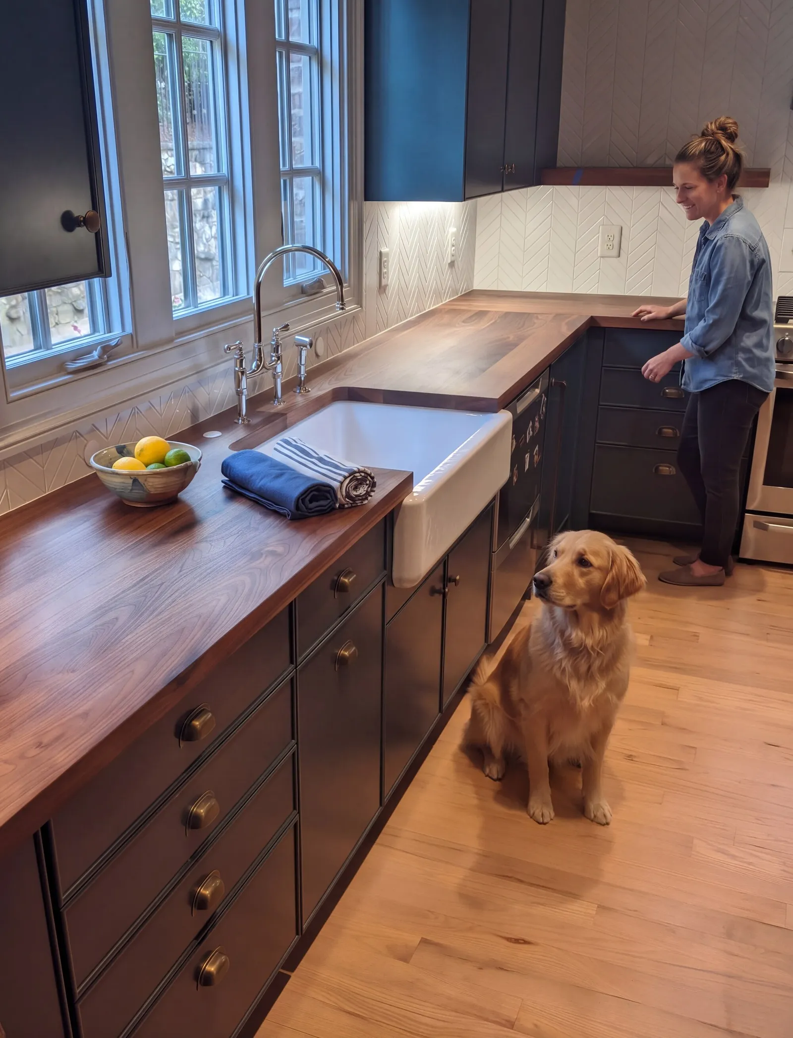 Walnut countertop along a scullery with dark cabinets and a farmhouse sink, a woman by the range and a golden retriever on the floor